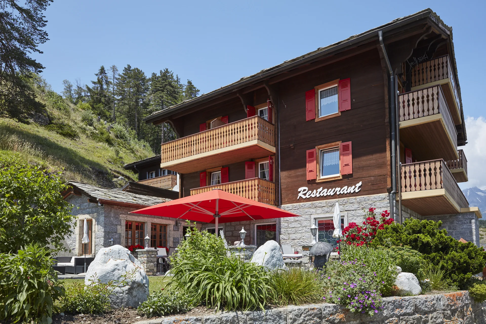 Jardin de l'hôtel avec terrasse, parasol rouge et verdure soignée