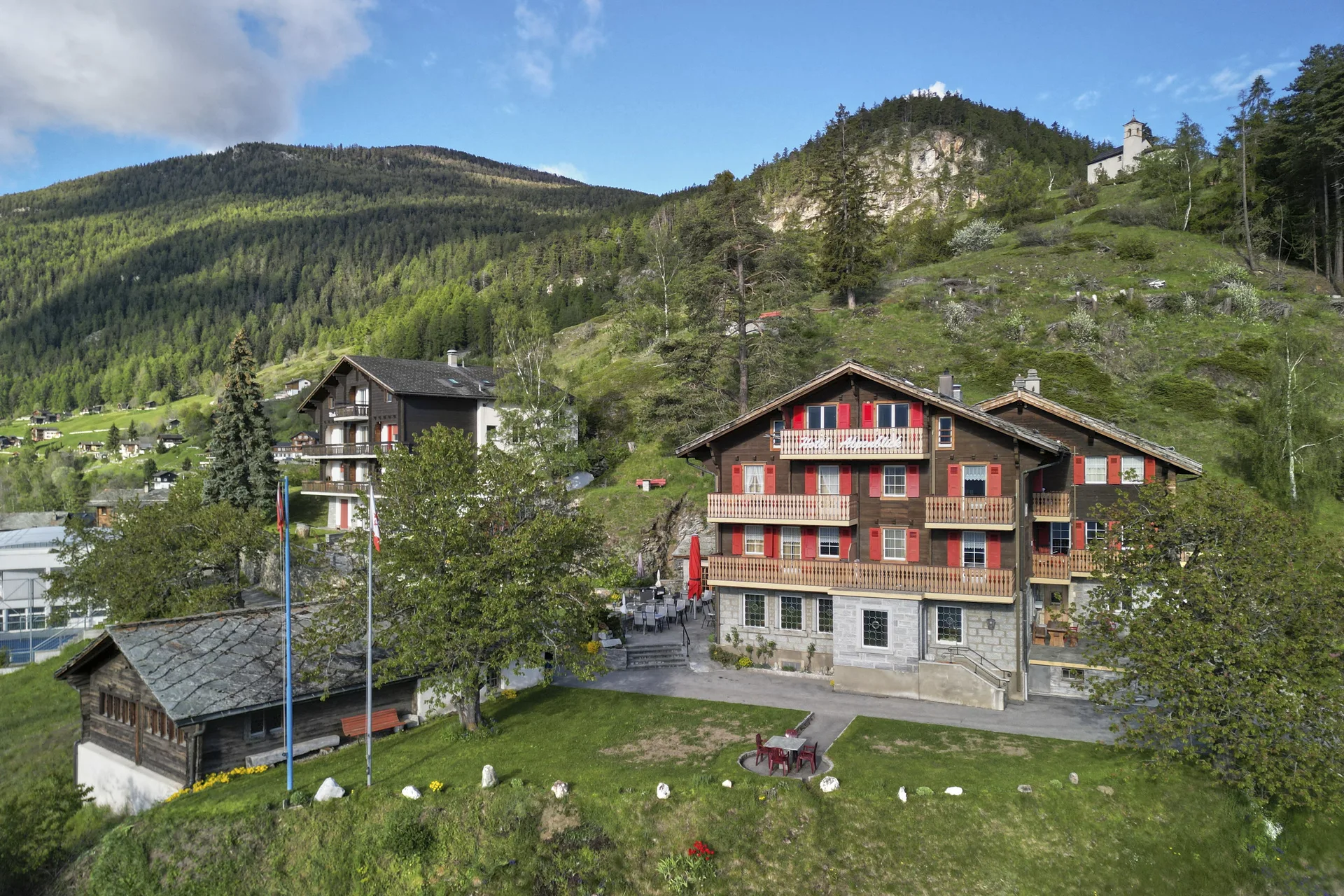 Luftaufnahme Hotel Alpenblick Zeneggen – Chalet mit roten Fensterläden im Alpendorf